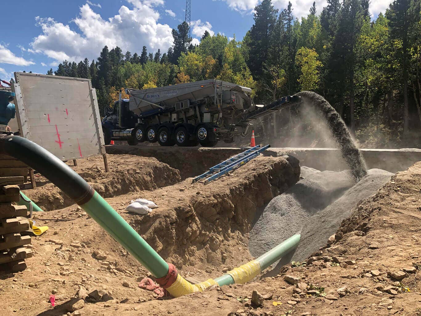 Bedrock slinger trucks backfilling with crusher fines around a natural gas pipeline in Colorado
